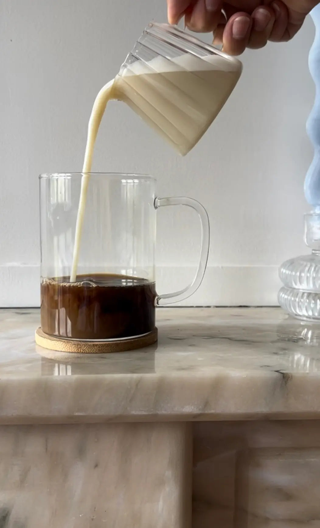 Pouring plant milk into a glass cup of Karobe, showing preparation for a caffeine-free carob latte or cappuccino.
