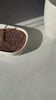 Video of a hand holding a white cup of Karobe roasted carob drink next to a bowl of carob powder, highlighting the rich color and coffee-like appearance, surrounded by carob beans.